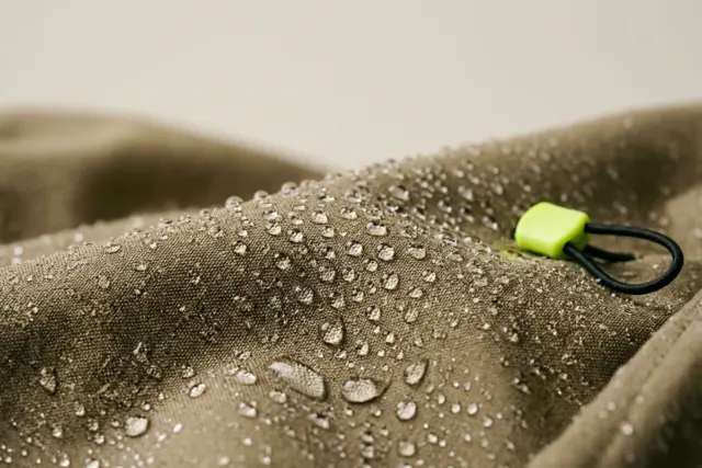 A macro close-up reveals tiny water droplets beading and rolling off the smooth, tightly woven khaki polyester fabric of a waterproof trench coat.