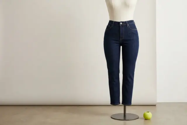 A pair of dark indigo stretch denim curvy-fit jeans, perfectly contoured to a neutral fabric dress form from the waist down, highlighting the absence of a waist gap, against a plain white wall.